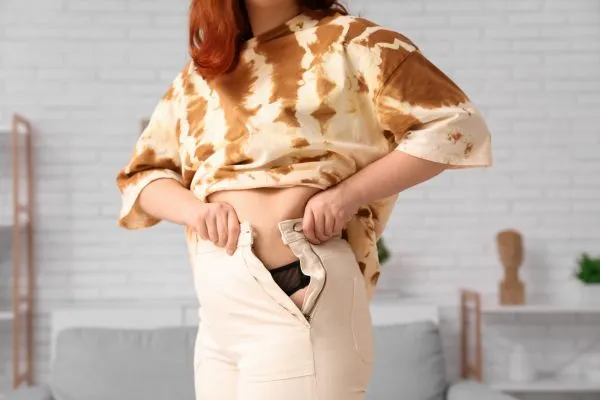 Image of woman trying to do her trousers up after pregnancy weight gain Newark