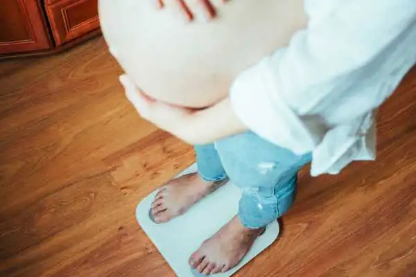 Image of woman weighing herself and experiencing weight gain through pregnancy Newark
